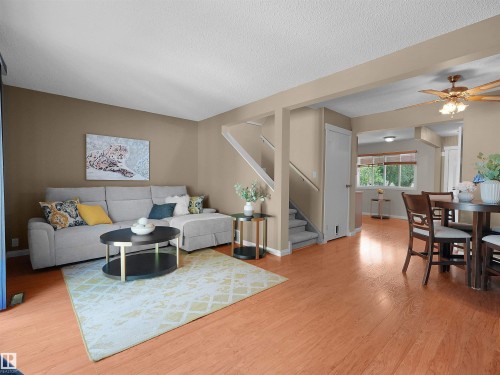 Open-concept living space featuring warm wood-finish flooring, neutral wall tones, a carpeted staircase, and a dining area with a ceiling fan - 16 13833 30 Street, Edmonton, AB 