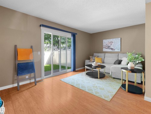 Living area with wood-finish flooring, neutral wall tones, and a large sliding glass door - 16 13833 30 Street, Edmonton, AB 