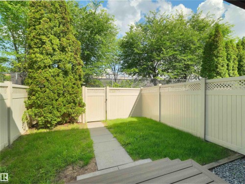 Private backyard featuring a manicured lawn, full-height privacy fencing with lattice accents, and a paved pathway leading to a gated entry - 16 13833 30 Street, Edmonton, AB 