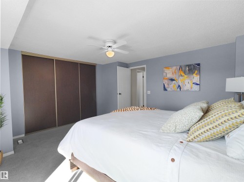 Spacious room featuring light gray carpeting, a multi-panel sliding closet with bronze frames, a white ceiling fan with integrated lighting, and light blue wall tones - 16 13833 30 Street, Edmonton, AB 