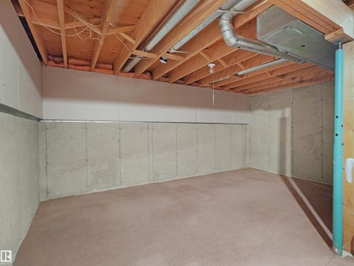 Unfinished basement featuring exposed wood joists, concrete foundation walls, and light-colored carpeting - 16 13833 30 Street, Edmonton, AB 