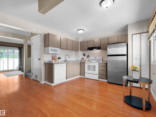 Kitchen featuring wood-finish flooring, full suite of appliances, neutral cabinetry, and a sliding glass door - 16 13833 30 Street, Edmonton, AB 