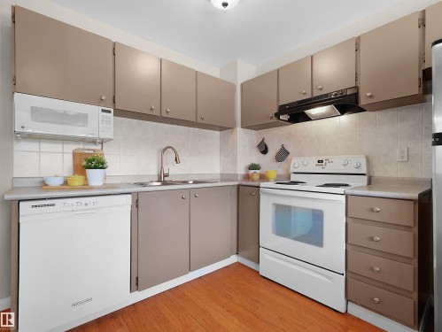 Functional kitchen featuring taupe cabinetry, white appliances, a double basin sink, light-colored tile backsplash, and wood-finish flooring - 16 13833 30 Street, Edmonton, AB 