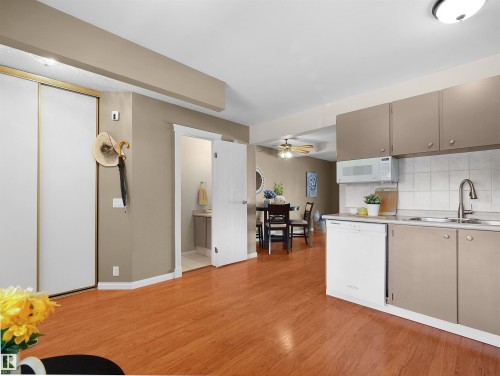 Open-concept living area featuring wood-finish flooring, a kitchen with neutral cabinetry and white tile backsplash, and a dining area with a ceiling fan - 16 13833 30 Street, Edmonton, AB 
