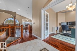 Open concept living area with vaulted ceilings, a prominent arched window, wood-finish flooring, a kitchen island with seating, and a dedicated office space with double French doors - 
