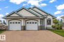 Front exterior featuring a dual-bay garage, stone accents, and an arched entry window - 215 Westerra Point(E), Stony Plain, AB 