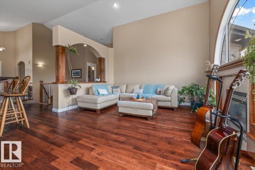 Spacious living area featuring rich wood-finish flooring, vaulted ceilings, and a large arched window with decorative mullions - 215 Westerra Point(E), Stony Plain, AB 