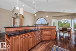 Kitchen and dining area featuring wood-finish flooring, rich wood cabinetry, dark countertops, an integrated cooktop, and vaulted ceilings with recessed lighting - 