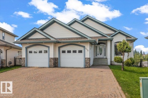 Two-car garage with arched doors, a brick paver driveway, white siding, stone accents, and a distinctive front entry - 215 Westerra Point(E), Stony Plain, AB 