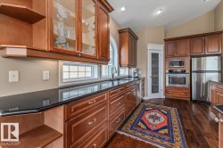 Kitchen featuring rich wood cabinetry, dark countertops, a built-in stainless steel oven and microwave, and an arched window above the sink - 