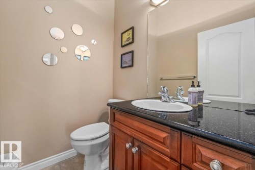 Bathroom vanity featuring a dark speckled countertop, an undermount sink with chrome fixtures, and rich wood-finish cabinetry - 215 Westerra Point(E), Stony Plain, AB 