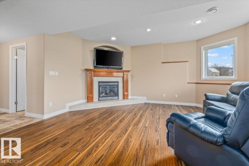 Living area featuring wood-finish flooring, a corner fireplace with a wood mantel, and a large window - 215 Westerra Point(E), Stony Plain, AB 
