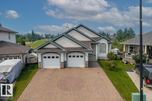 Split-level residence featuring a two-car garage with stone detailing, a patterned paver driveway, and a manicured front lawn - 215 Westerra Point(E), Stony Plain, AB 