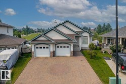 Split-level residence featuring a two-car garage with stone detailing, a patterned paver driveway, and a manicured front lawn - 