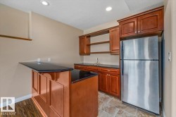 Wet bar featuring an extended countertop, rich wood cabinetry, stainless steel refrigerator, and recessed lighting - 