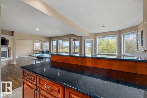 Lower level entertaining space featuring a black speckled countertop, rich wood-finish cabinetry, a bay window configuration, and wood-finish flooring - 215 Westerra Point(E), Stony Plain, AB 