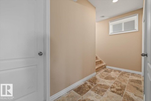 Hallway featuring large format tiled flooring, a window with horizontal blinds, and a staircase with coordinated tile risers - 215 Westerra Point(E), Stony Plain, AB 