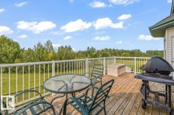 Spacious wood-finish deck with white railings, featuring an expansive green landscape backdrop - 