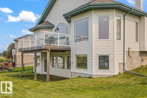 Exterior featuring a raised deck with white railing, a ground-level patio door, and multiple windows across two levels - 215 Westerra Point(E), Stony Plain, AB 