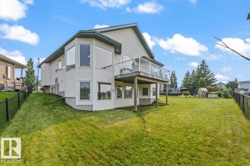 Expansive fenced backyard featuring a manicured lawn, an elevated deck with white railings, and a walk-out lower level - 215 Westerra Point(E), Stony Plain, AB 