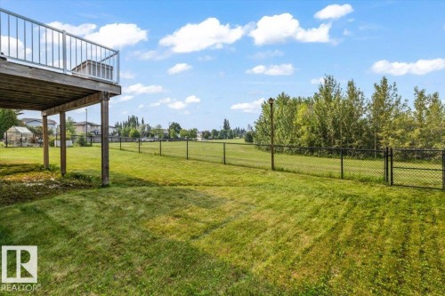 Expansive backyard featuring a manicured lawn, established trees, and perimeter chain link fencing - 215 Westerra Point(E), Stony Plain, AB 