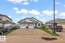 Ranch-style residence featuring a two-car garage with arched doors, stone veneer accents, and a gabled roofline - 