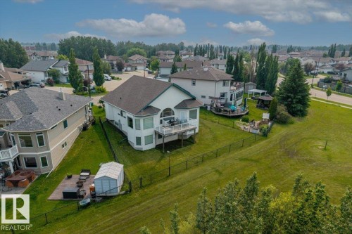 Expansive green space featuring a fenced yard, mature trees, and a multi-level deck - 215 Westerra Point(E), Stony Plain, AB 
