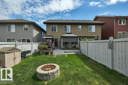 Expansive backyard featuring a manicured lawn, a built-in stone fire pit, and a spacious deck - 6042 214 Street, Edmonton, AB - Outdoor With Deck Patio Veranda With Exterior