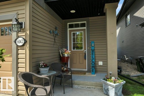 Inviting front entry featuring a covered porch, durable siding, a wood-finish door with transom window, and an exterior light fixture - 6042 214 Street, Edmonton, AB - Outdoor With Deck Patio Veranda With Exterior