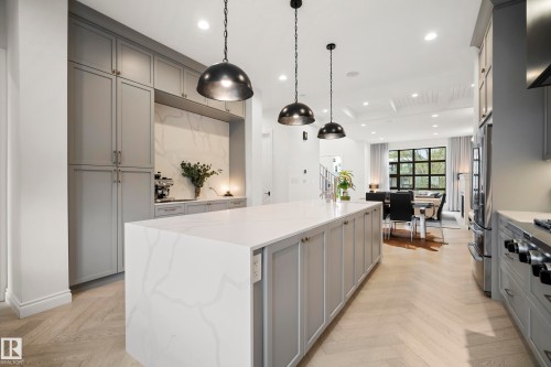 Expansive kitchen island featuring a waterfall countertop with veining, grey shaker cabinetry, and three pendant lights - 6115 111 Avenue, Edmonton, AB - Indoor Photo Showing Kitchen With Upgraded Kitchen