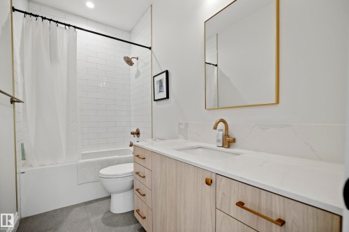 Bathroom featuring a light wood-finish vanity with a white countertop and integrated sink, a rectangular gold-framed mirror, and brass-finish fixtures - 6115 111 Avenue, Edmonton, AB - Indoor Photo Showing Bathroom