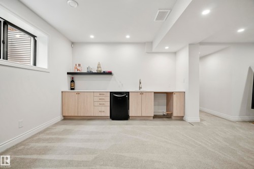 Lower-level entertainment space featuring a wet bar with light wood-finish cabinetry, a black beverage refrigerator, and a white countertop - 6115 111 Avenue, Edmonton, AB - Indoor