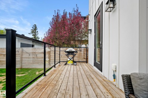 Outdoor deck with natural wood-finish flooring, glass panel railing, and black metal posts - 6115 111 Avenue, Edmonton, AB - Outdoor With Deck Patio Veranda With Exterior