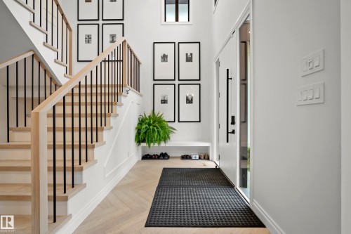 Two-story entryway featuring a light wood-finish staircase with black metal balusters and a contrasting dark wood-finish front door - 6115 111 Avenue, Edmonton, AB - Indoor Photo Showing Other Room
