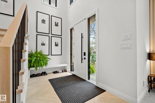 Entry foyer featuring a tall ceiling, light wood-finish herringbone flooring, a modern white door with a vertical glass panel and matte black hardware, and a light wood staircase with black metal balusters - 6115 111 Avenue, Edmonton, AB - Indoor Photo Showing Other Room