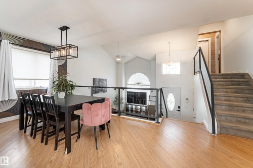 Open-concept interior featuring wood-finish flooring, a contemporary chandelier, a glass and metal railing system, and a vaulted ceiling with an arched window - 183 Dechene Road, Edmonton, AB 