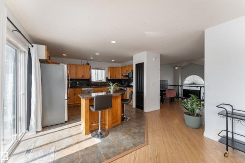 Kitchen featuring wood cabinetry, stainless steel appliances, a tile backsplash, and an island with seating - 183 Dechene Road, Edmonton, AB 