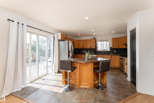Kitchen featuring wood cabinetry, stainless steel appliances, black subway tile backsplash, and a granite island with seating - 183 Dechene Road, Edmonton, AB 