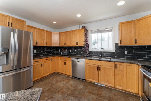 Kitchen with wood-finish cabinetry, stainless steel appliances, and dark subway tile backsplash - 183 Dechene Road, Edmonton, AB 