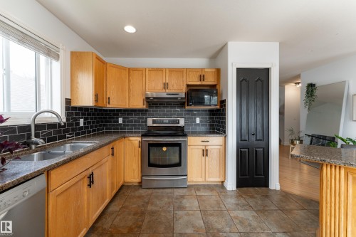 Kitchen featuring natural wood cabinetry, dark subway tile backsplash, stainless steel appliances, and granite-style countertops - 183 Dechene Road, Edmonton, AB 