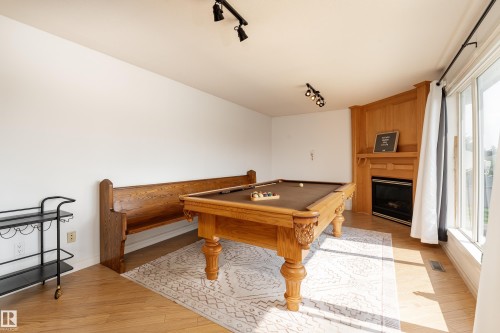 Bright room featuring wood-finish flooring, a corner fireplace with a light wood mantel, and large windows with white trim - 183 Dechene Road, Edmonton, AB 