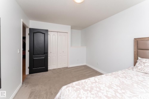 Carpeted room featuring a ceiling-mounted light fixture, white baseboards, a dark paneled interior door, and bi-fold closet doors - 183 Dechene Road, Edmonton, AB 