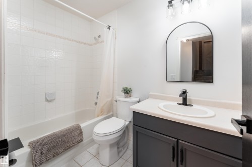 Bathroom featuring a white subway tile tub surround, a black arched mirror, a vanity with a white countertop and dark gray cabinetry, and a black faucet - 183 Dechene Road, Edmonton, AB 