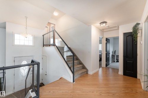 Two-story entryway featuring wood-finish flooring, a contemporary glass and metal railing staircase, and a white front door with an oval decorative glass insert - 183 Dechene Road, Edmonton, AB 
