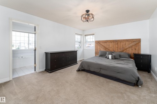 Carpeted room featuring a rustic wood headboard, two windows, and an overhead light fixture - 183 Dechene Road, Edmonton, AB 
