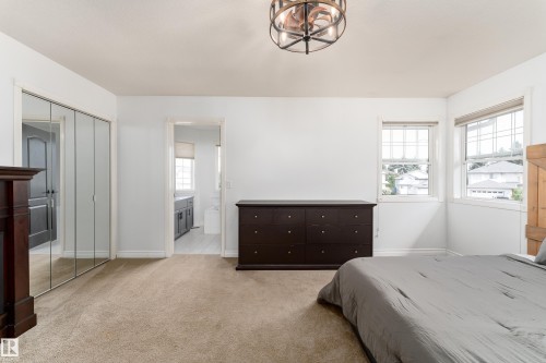 Carpeted room featuring multiple windows, a decorative ceiling light fixture, mirrored closet doors, and an open doorway revealing a bathroom with wood-finish cabinetry - 183 Dechene Road, Edmonton, AB 