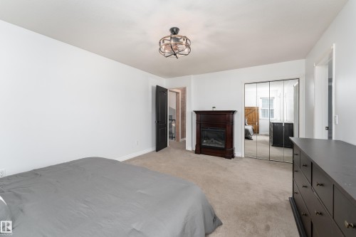 Carpeted bedroom featuring a dark wood mantle with an electric fireplace insert, mirrored closet doors, and a ceiling-mounted light fixture - 183 Dechene Road, Edmonton, AB 