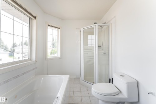 Bathroom featuring a corner shower enclosure, white built-in tub, and two windows with grilles - 183 Dechene Road, Edmonton, AB 