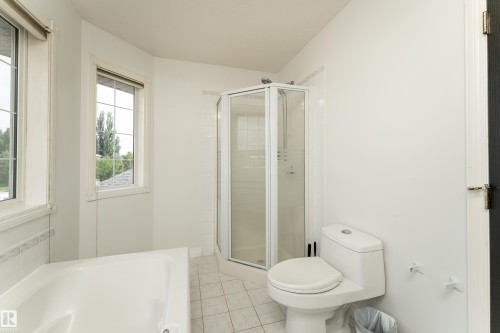 Bathroom featuring a built-in tub, corner glass-enclosed shower, and a window with grid patterns - 183 Dechene Road, Edmonton, AB 
