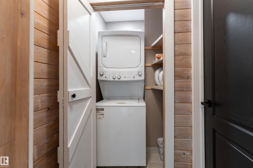 Integrated laundry closet featuring a stacked white washer and dryer, wood-finish wall paneling, and built-in shelving - 183 Dechene Road, Edmonton, AB 